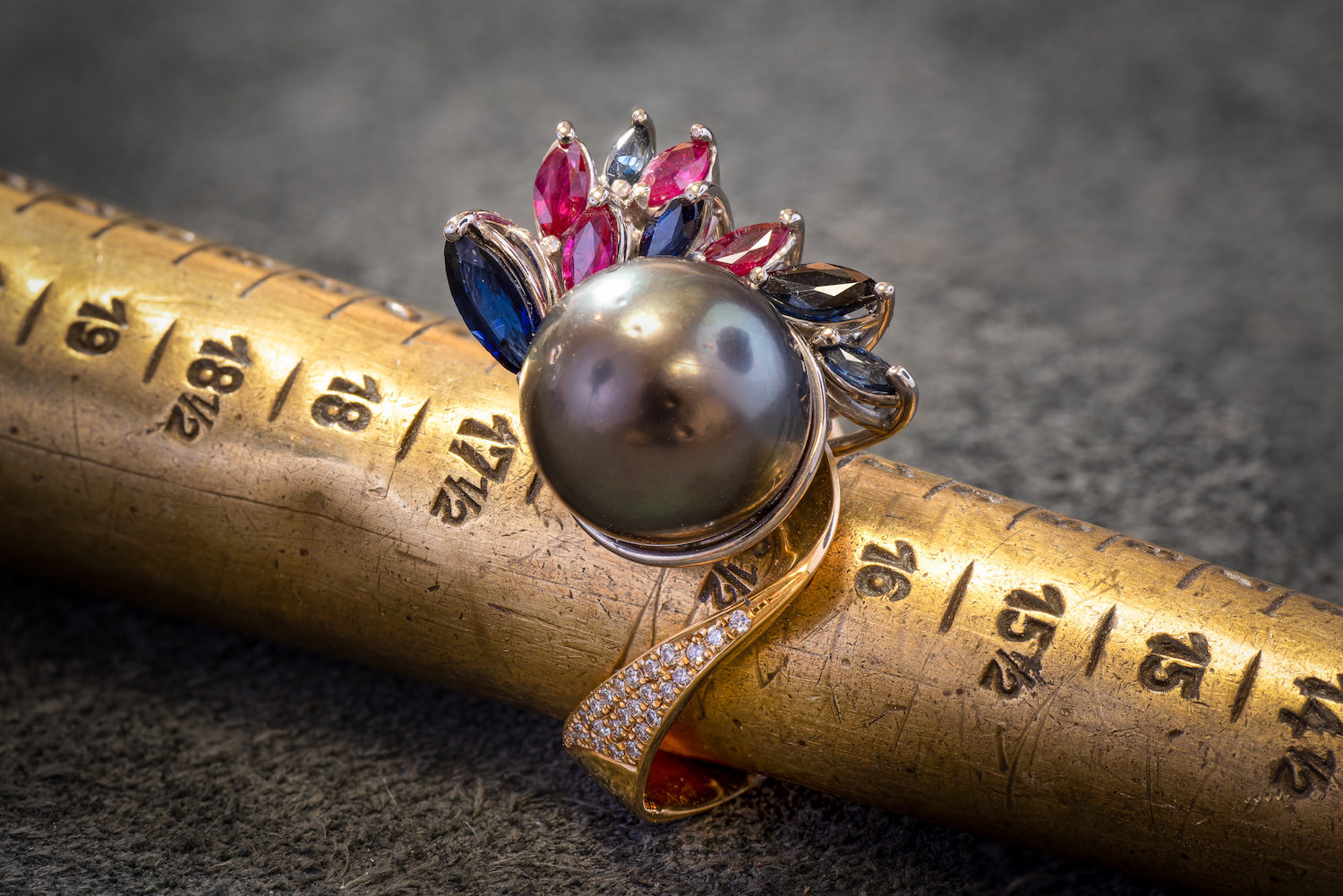 Ring mit dunkler Perle und farbigen Edelsteinen auf einem Ringmaß